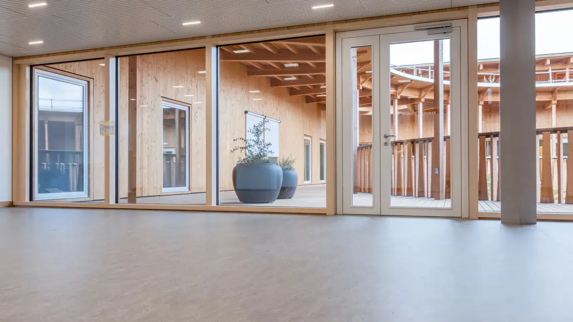 Lichtgrijze linoleumvloer in de entree van een kinderopvang, met natuurlijke lichtinval en kindvriendelijke inrichting.