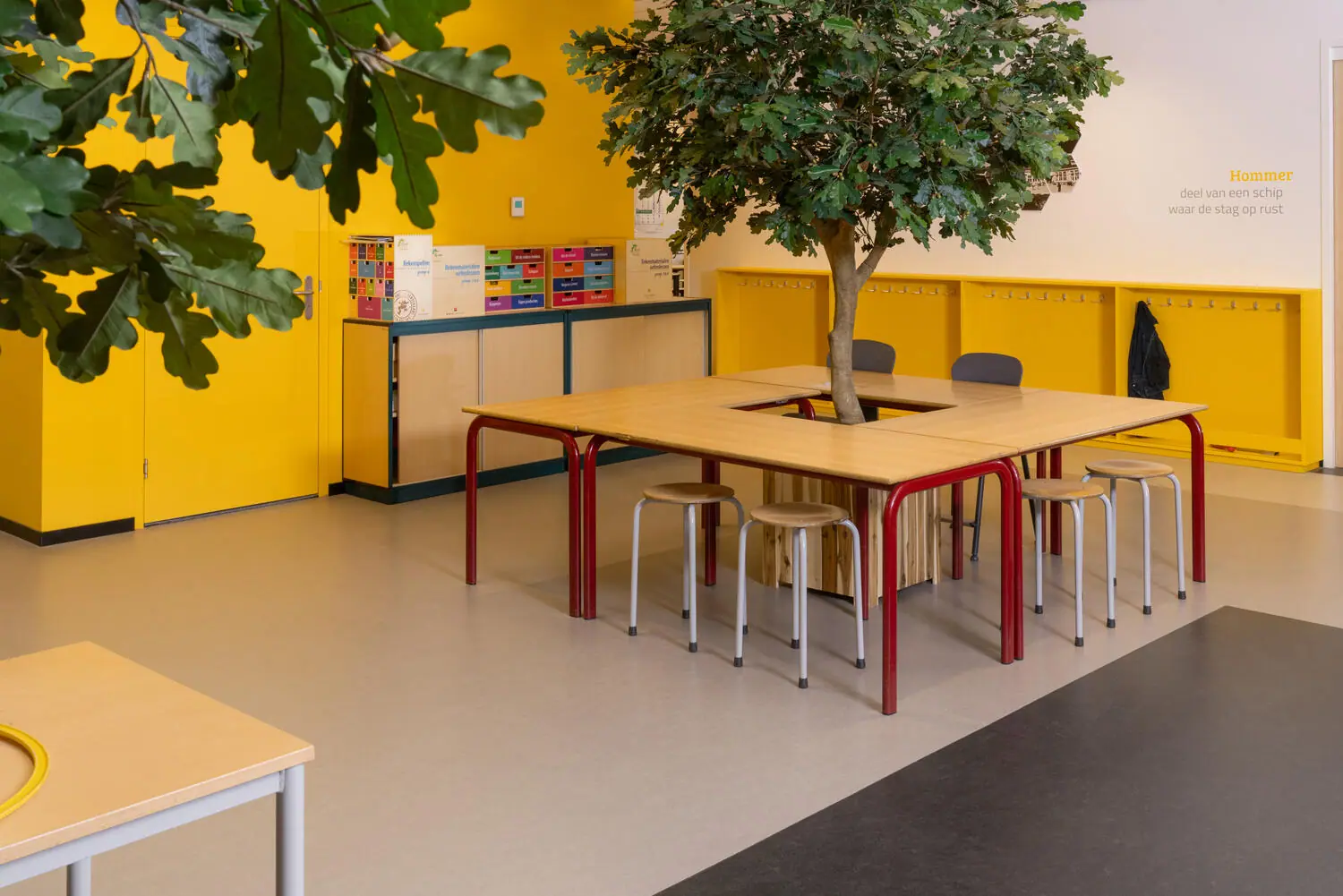 Lichte linoleumvloer in een schoolruimte met houten tafels en een boom