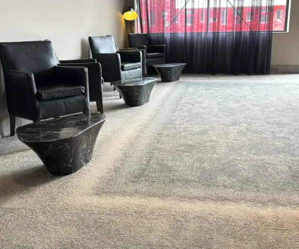 Lichtgrijs tapijt met rand in een lounge met zwarte fauteuils