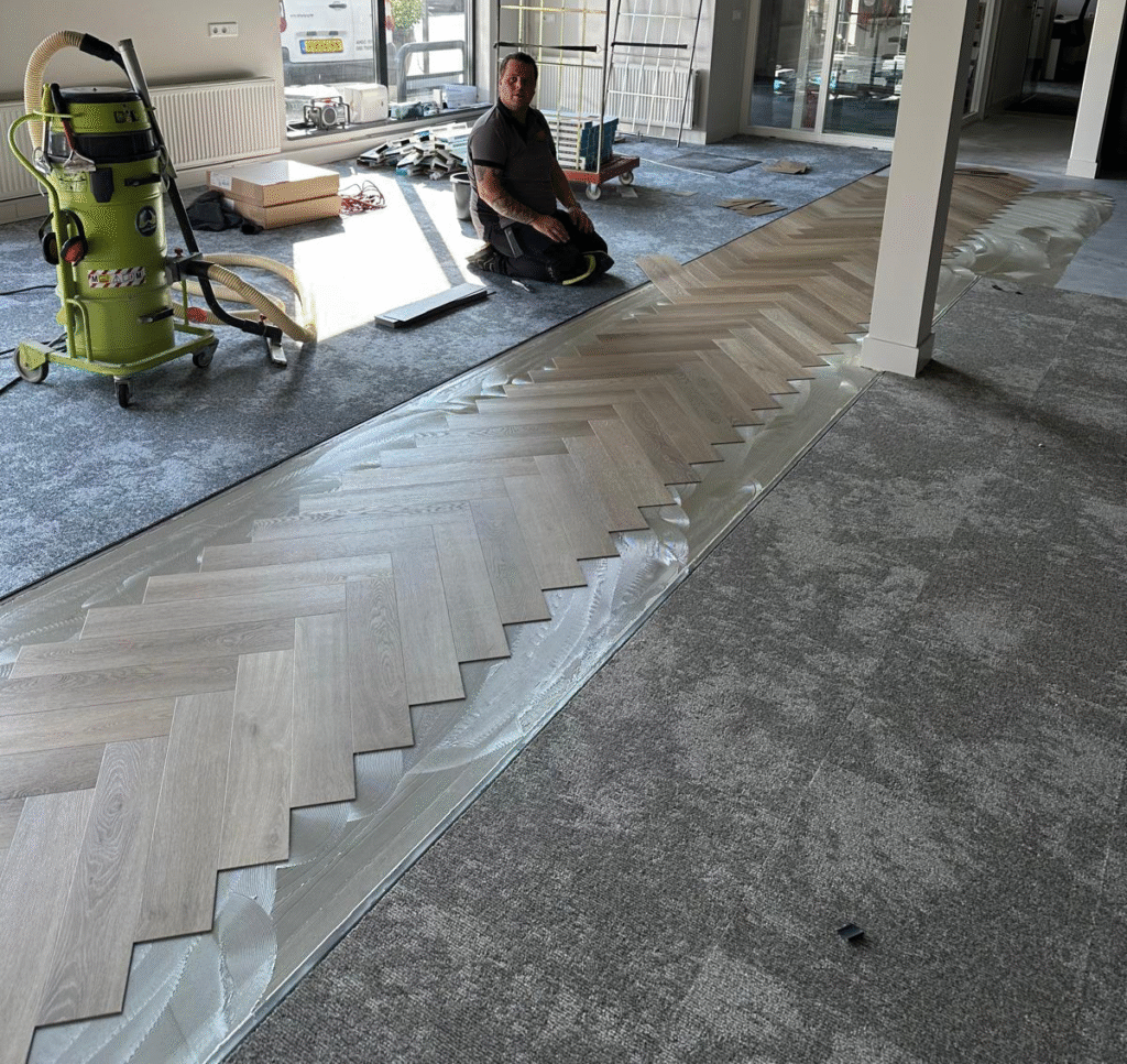 Een vakman brengt zorgvuldig vloerbedekking aan in een moderne zakelijke ruimte met behulp van professionele gereedschappen.